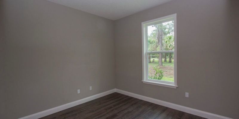 Empty beige bedroom with gray carpet and a window looking out onto greenery.