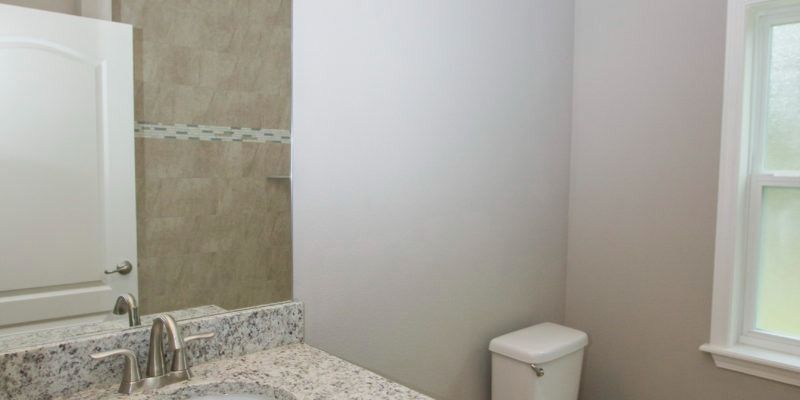Bathroom with granite vanity, tiled shower, toilet, and window in a bright neutral room