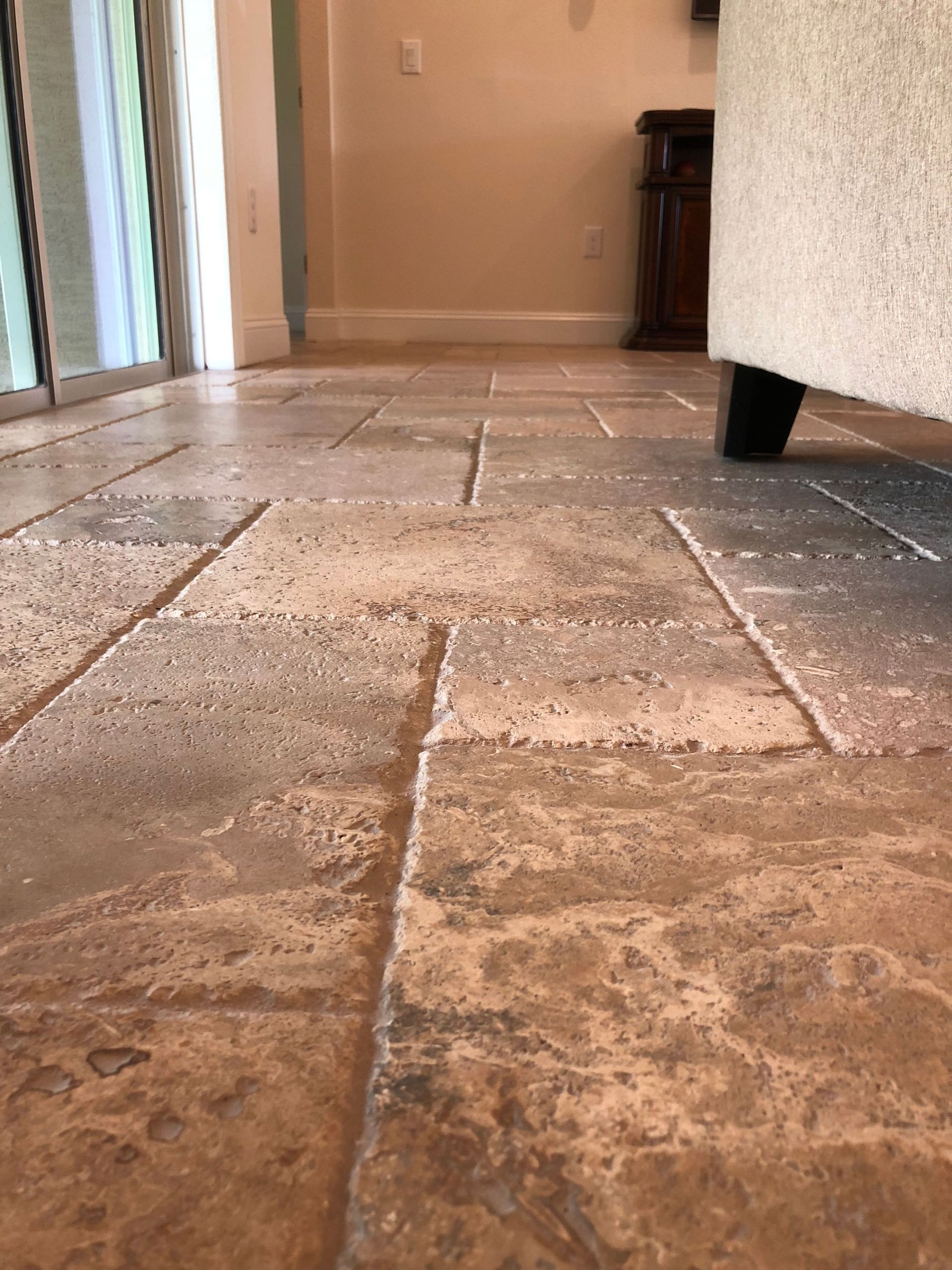 Low-angle view of a tiled indoor floor with a couch and doorway in the background
