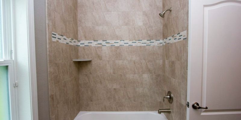 Empty tiled shower with built-in shelf and handheld showerhead.