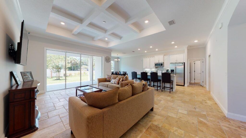 Bright open-concept living room with tan sofa, dining table, tile floor, and large sliding glass doors