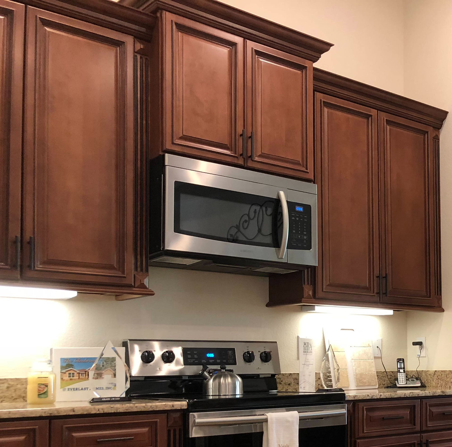 Kitchen with dark wood cabinets, stainless steel microwave and stove, and under-cabinet lighting.