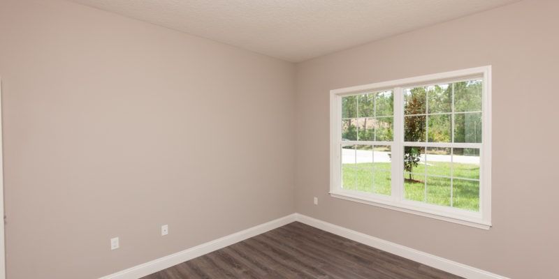 Empty beige bedroom with gray carpet and a window overlooking a green yard