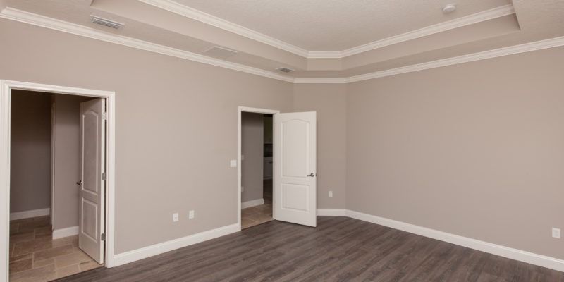 Empty beige bedroom with tray ceiling, hardwood floor, and two open doorways