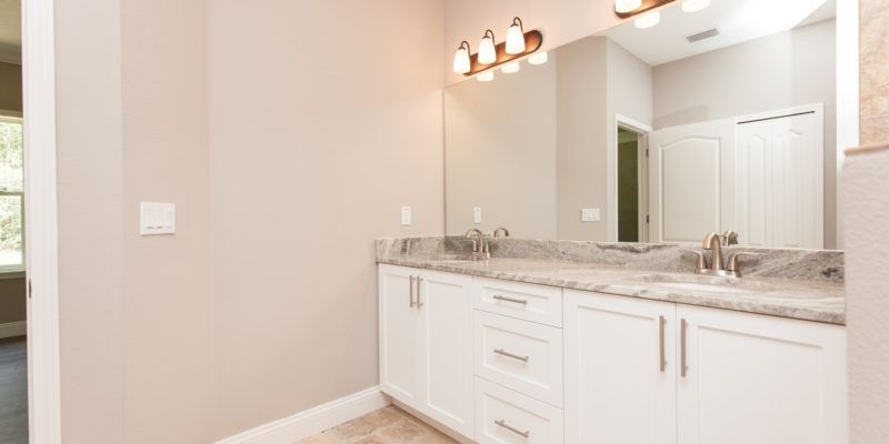 Bright bathroom vanity with white cabinets, marble countertop, large mirror, and overhead lights