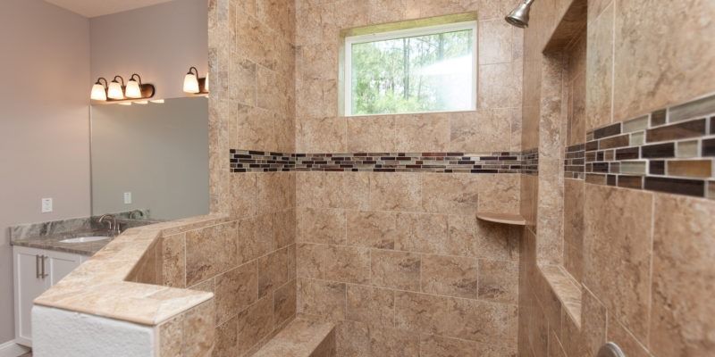 Large beige tiled walk-in shower with glass block walls and a small window