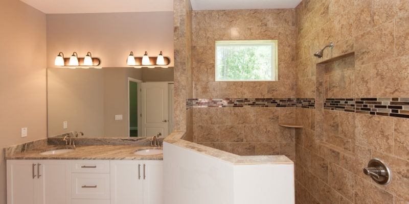 Spacious beige bathroom with double vanity, large mirror, and tiled walk-in shower with glass wall