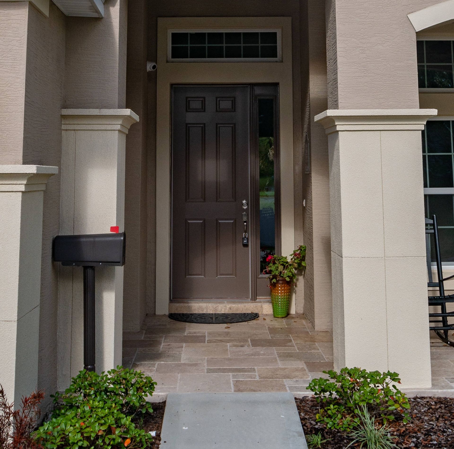 Front porch with dark wooden front door, beige columns, mailbox, and potted flowers by the entryway