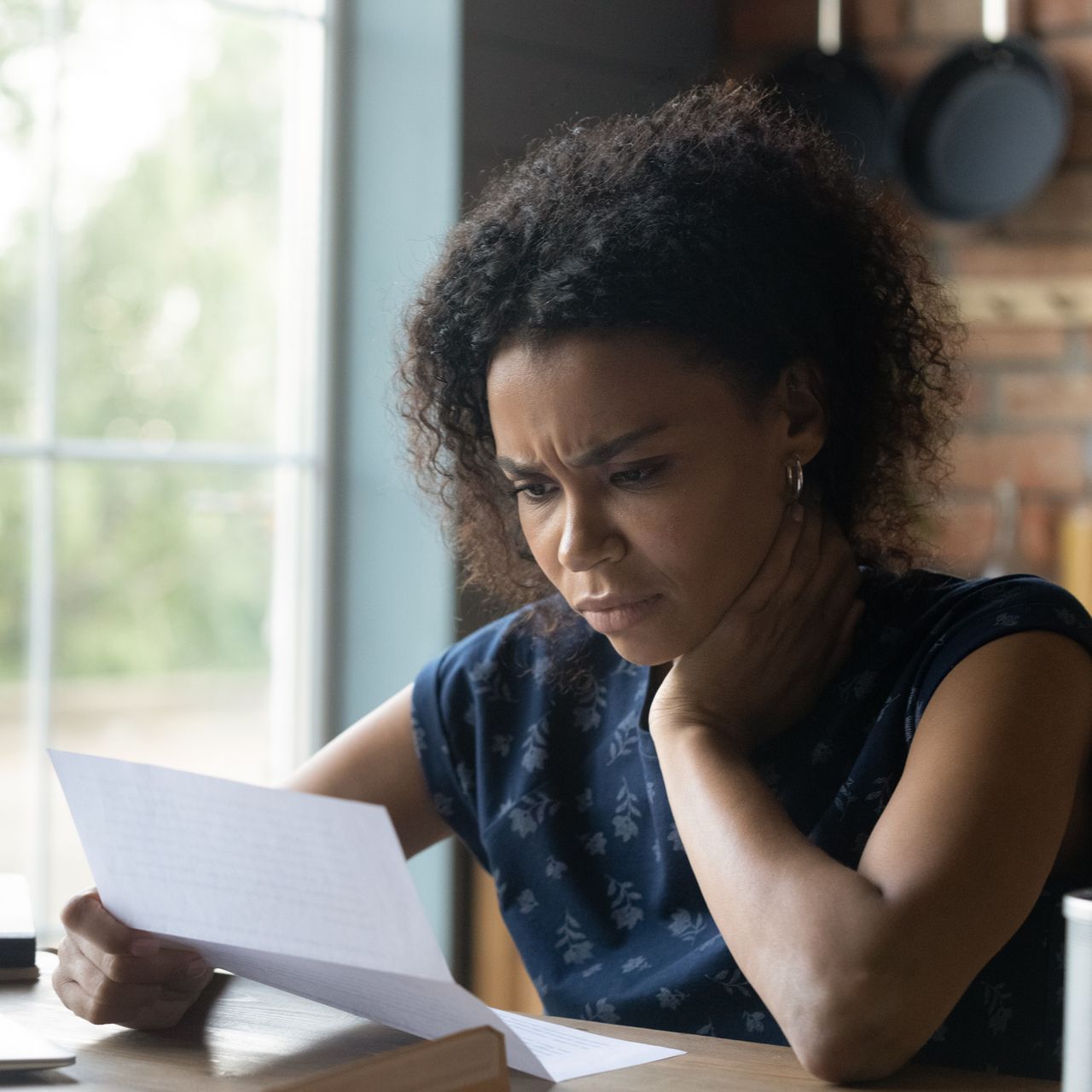 A woman is sitting at a table reading a piece of paper.