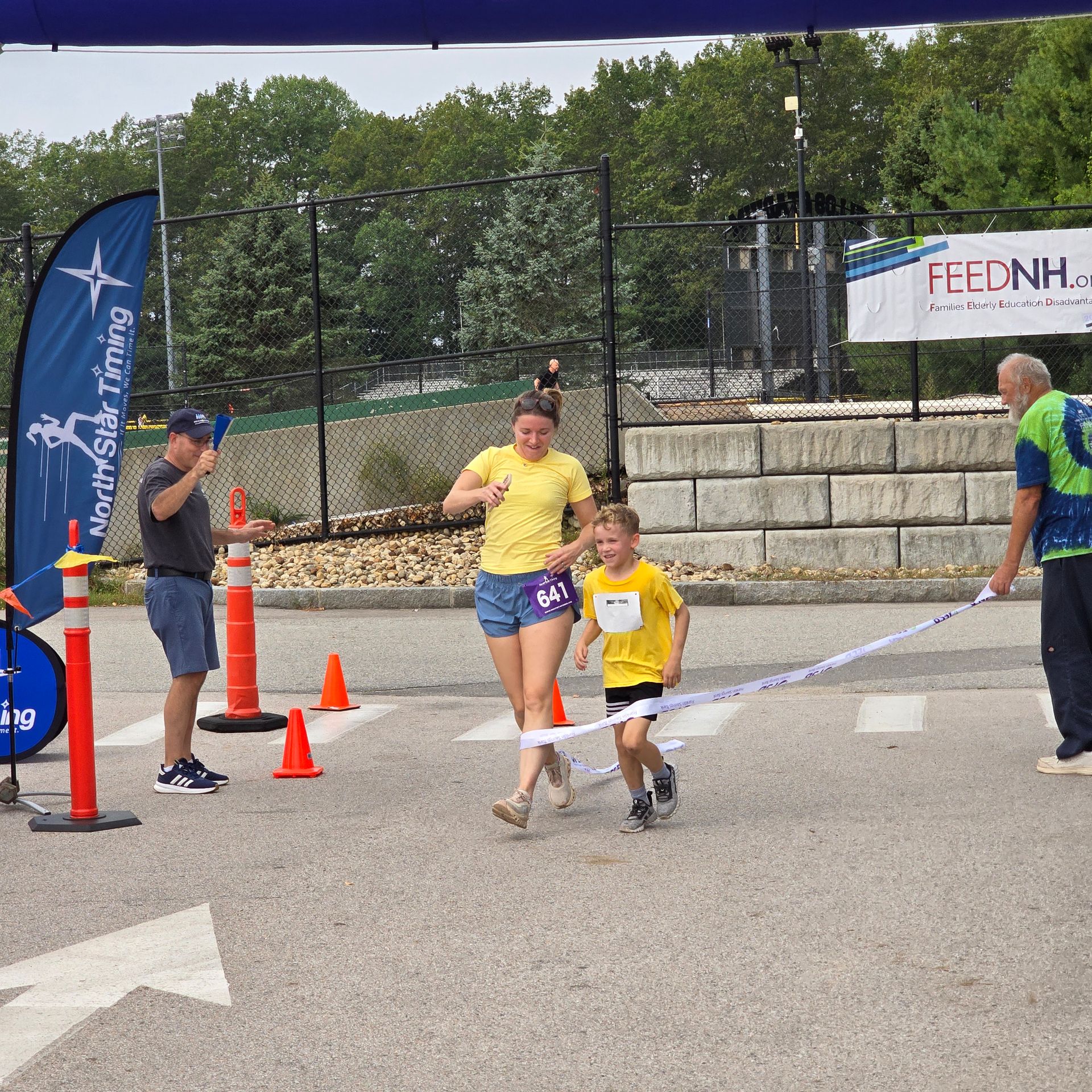 Man in orange shirt and boy in gold shirt running race. Outdoors on sunny day.