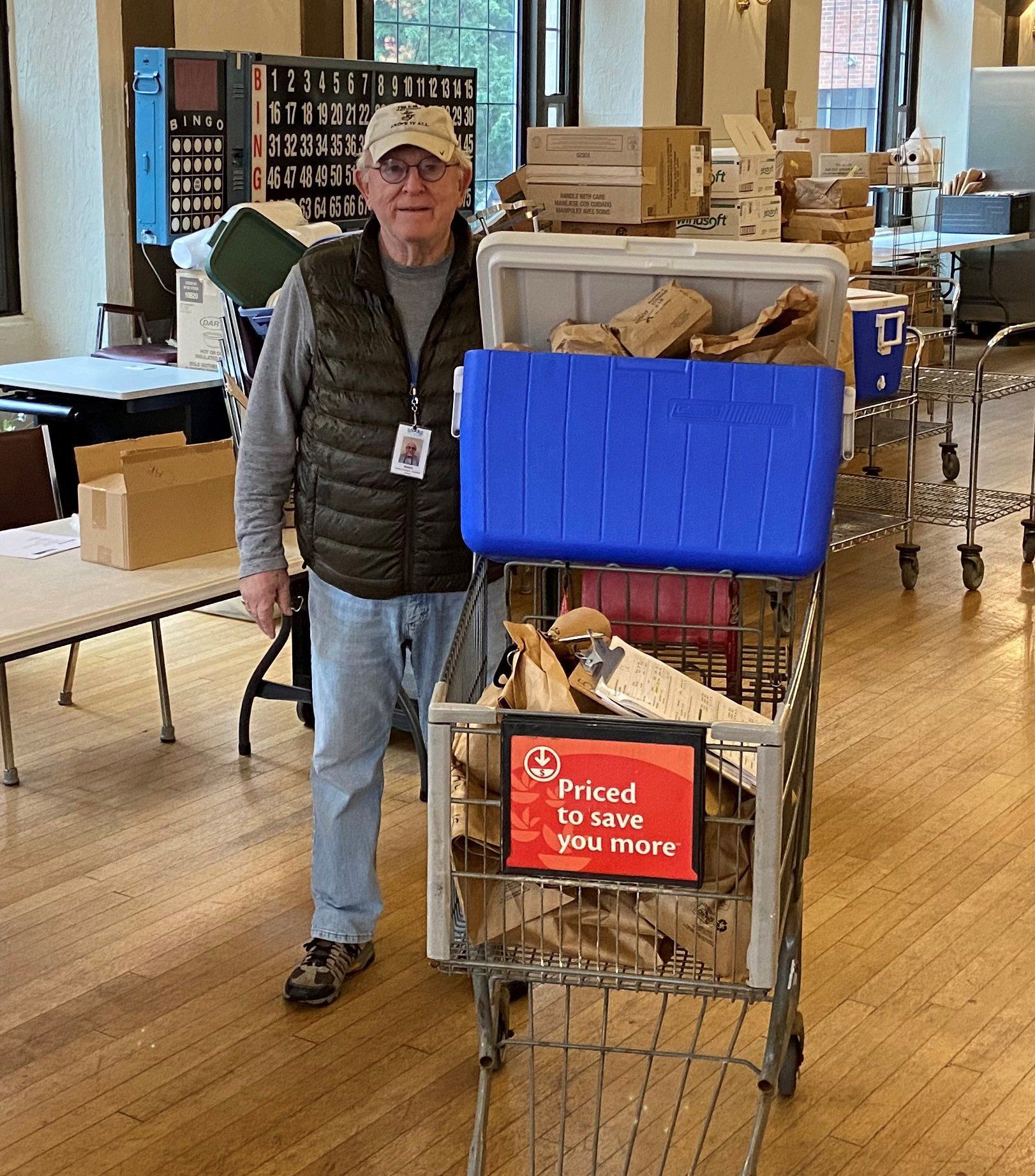 Man standing by shopping cart full of supplies indoors, possibly at a donation center.