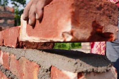 Mason is laying red bricks onto fresh mortar on a wall under construction. Mason is laying red bricks onto fresh mortar on a wall under construction.