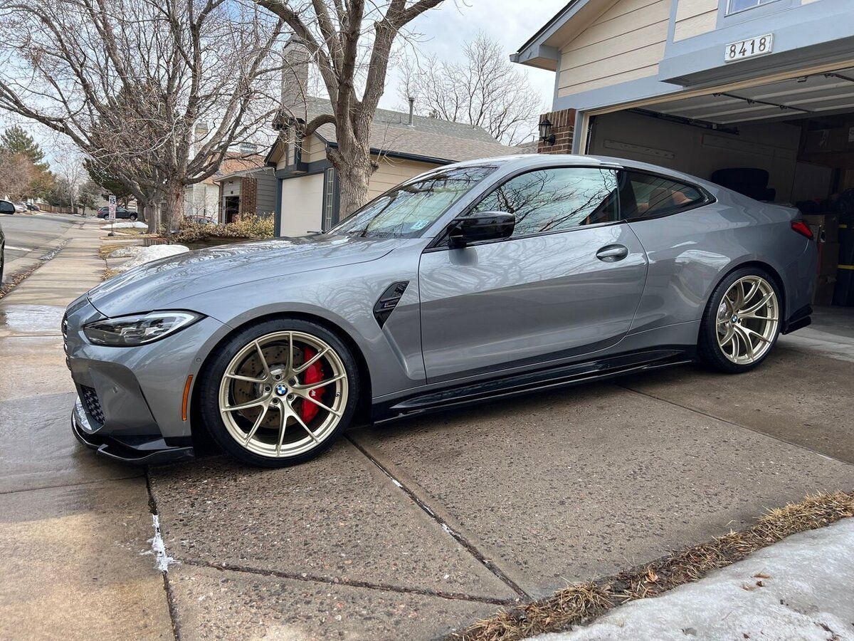 A gray bmw m4 is parked in front of a garage.