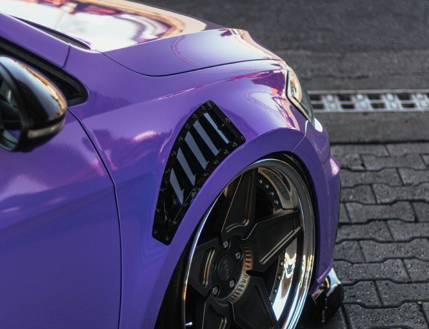 A purple car is parked on a brick sidewalk.