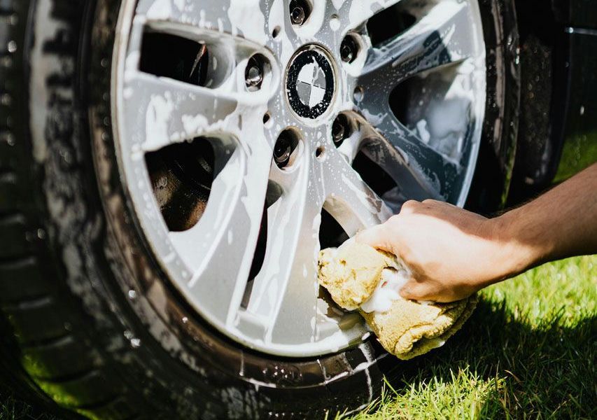 A person is washing a car wheel with a sponge.