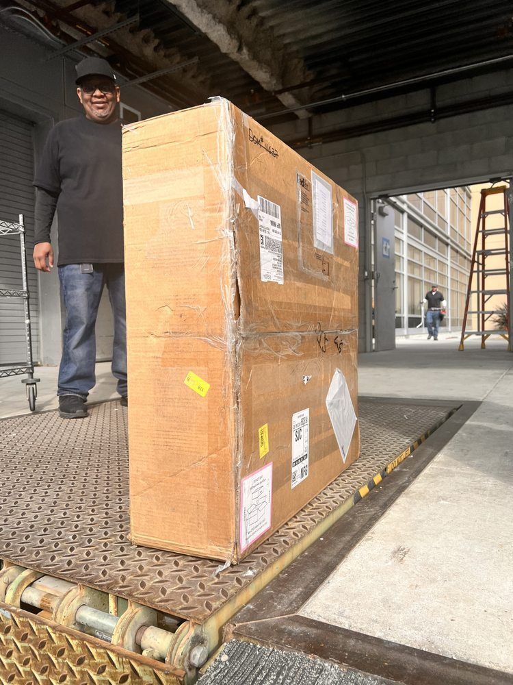 A man is carrying a large cardboard box on a conveyor belt.