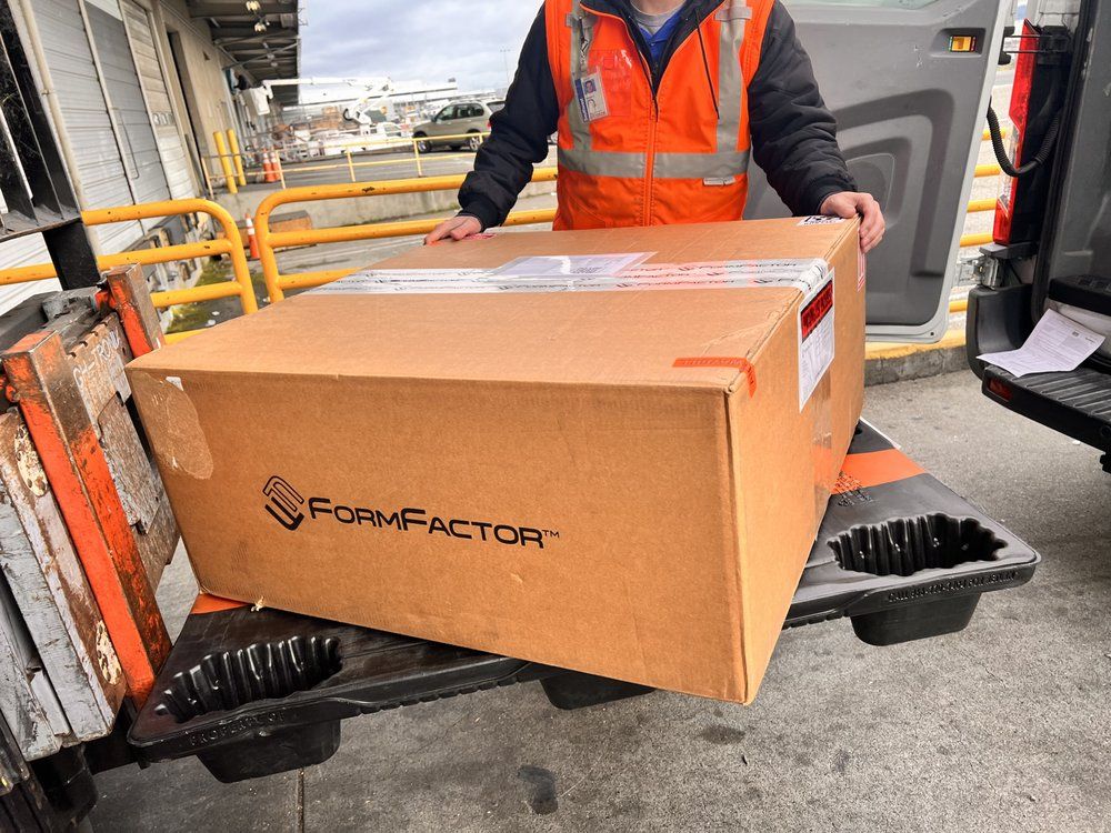 A man in an orange vest is holding a large cardboard box.