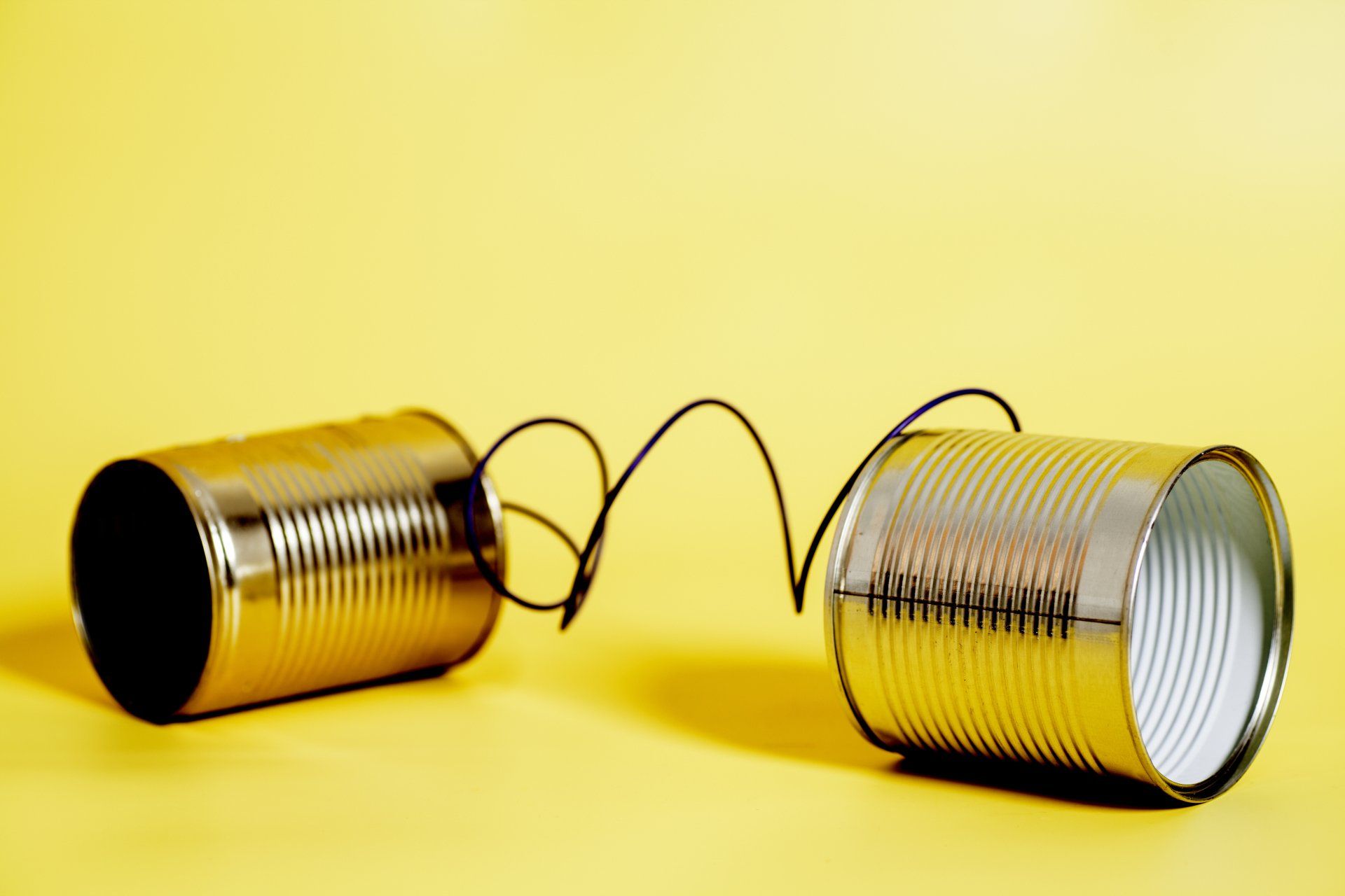 2 tinnen blikjes met een draad er tussen op een gele achtergrond. Communicatie.