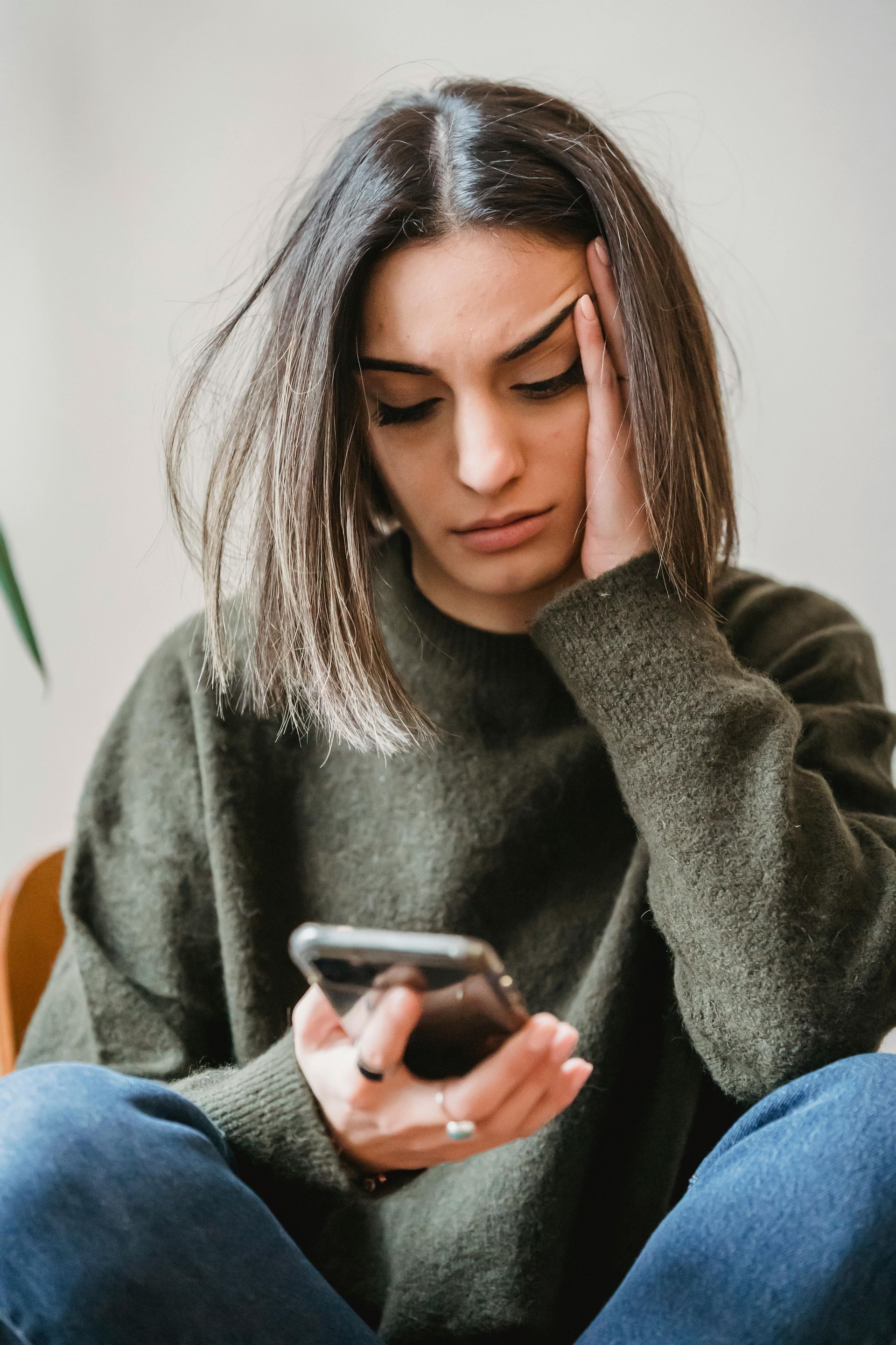 Woman holding phone, looking down with concerned expression, hand on forehead.