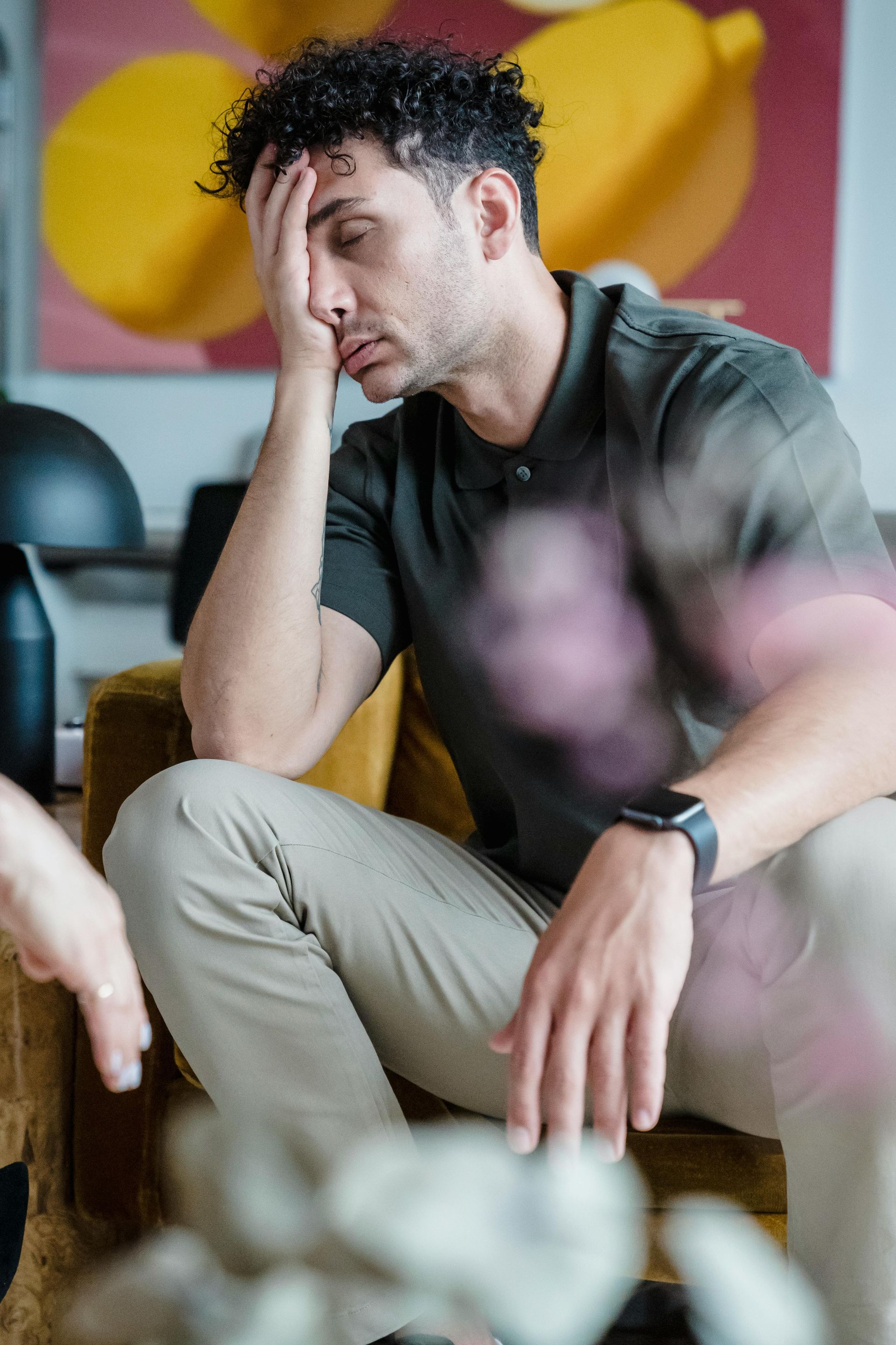 Man in a green shirt and khaki pants, resting his head. He sits on a yellow chair, facing burnout and anxiety.