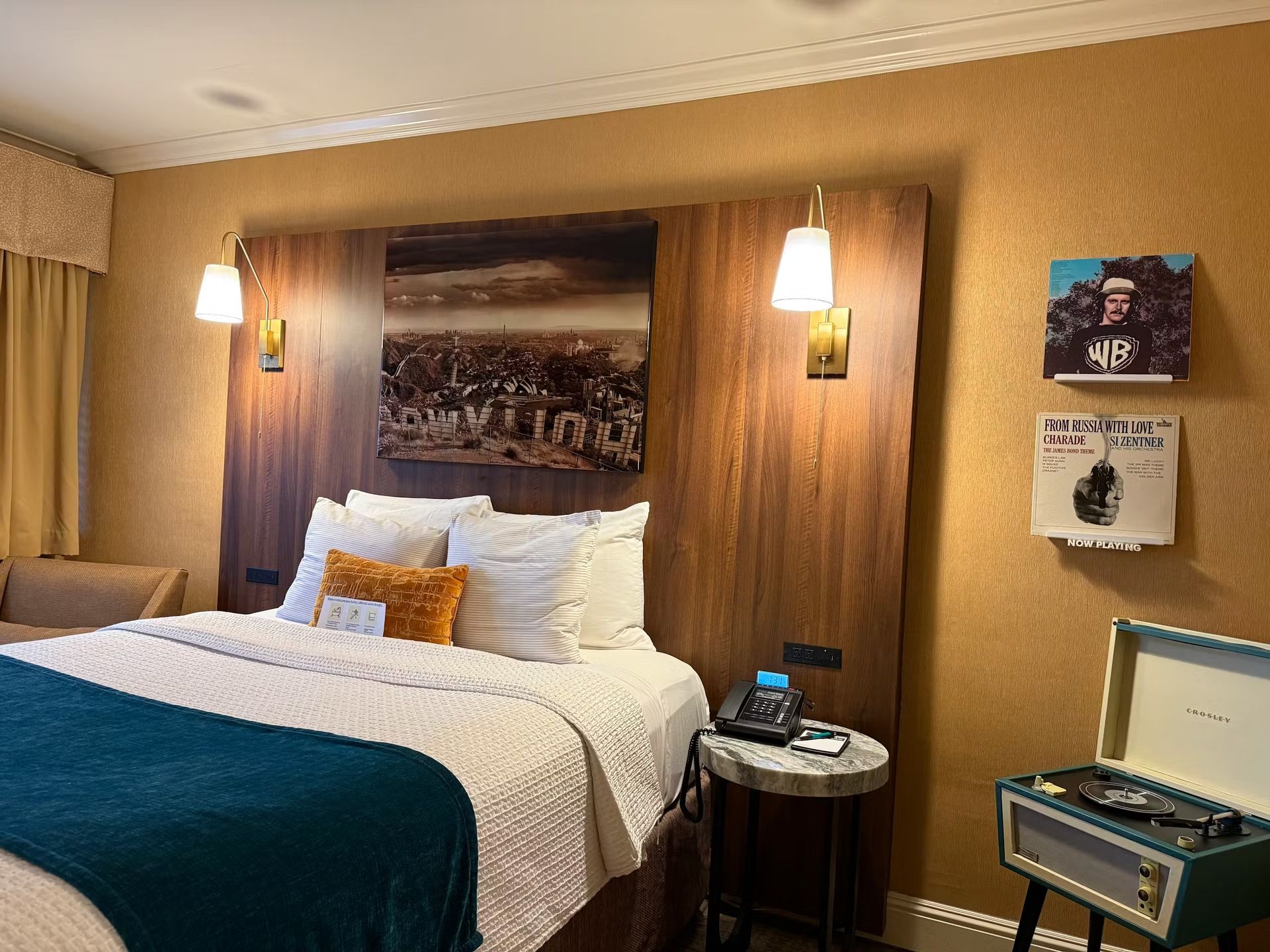 A hotel bed with white linens and a teal throw, set against a wood headboard.