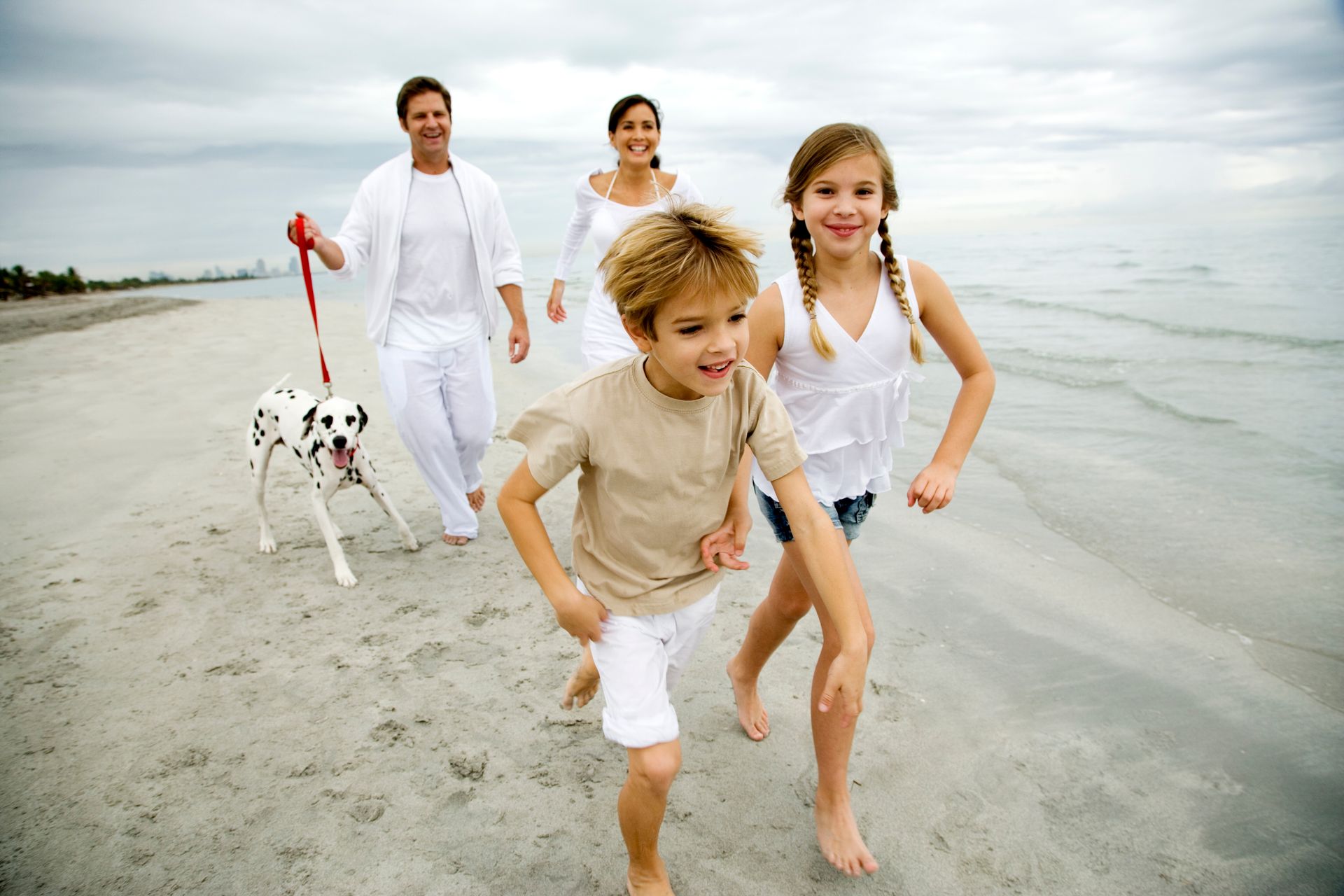 Family walking barefoot with a spotted dog on a beach at the shoreline