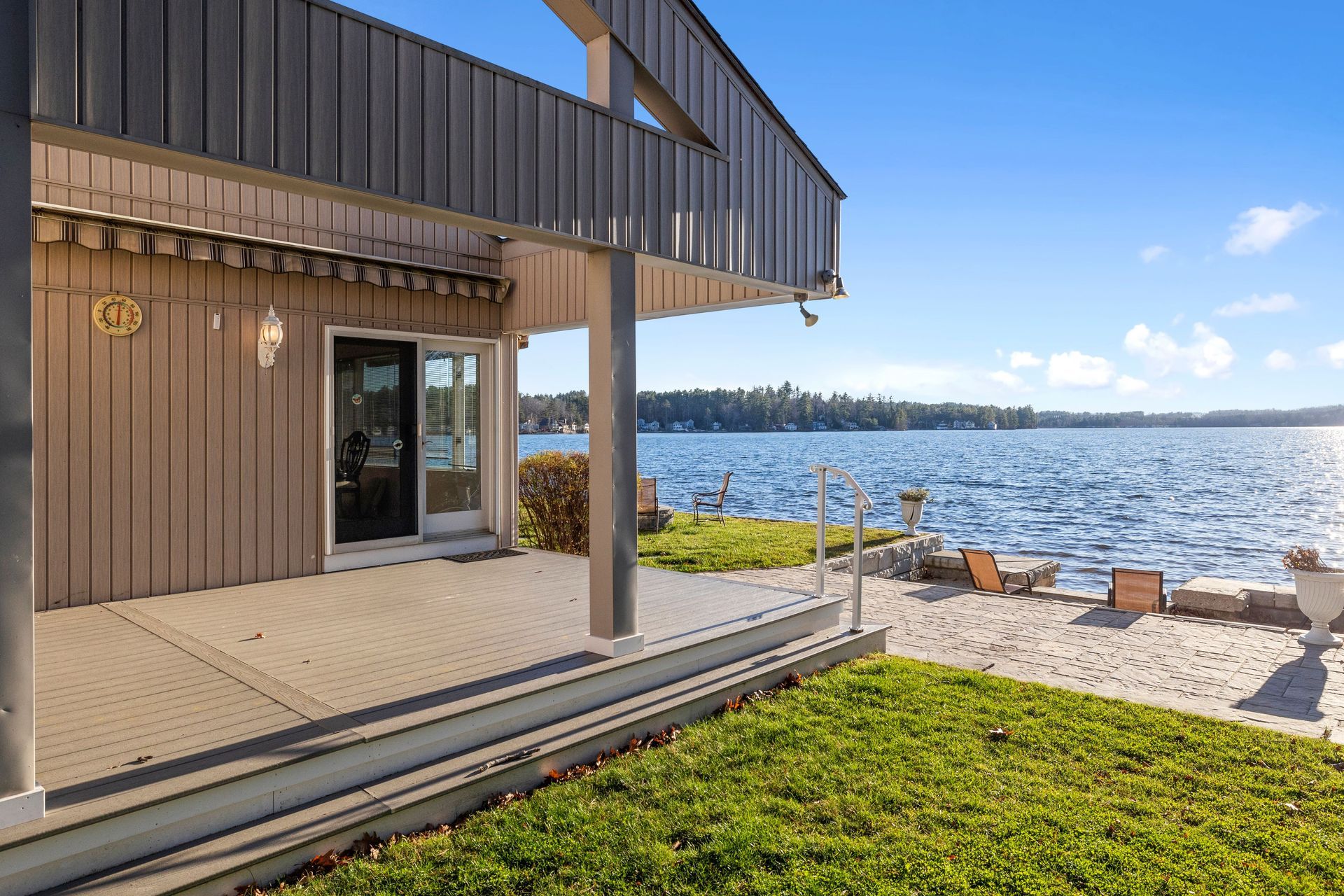 Modern lakeside house deck with grass, patio chairs, and water view under a clear blue sky