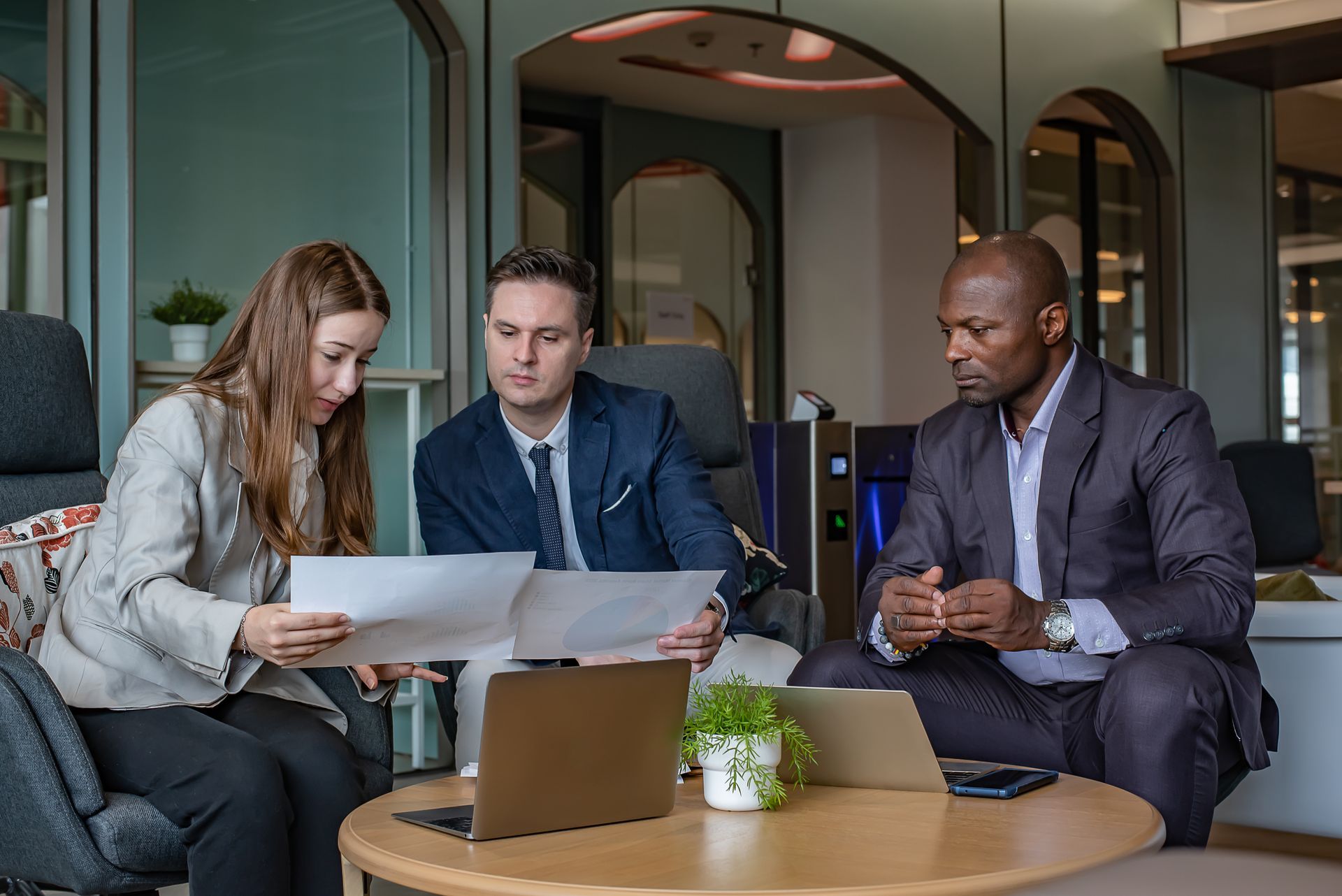 Two coworkers discussing a laptop in a modern office, with documents and a phone on the desk.