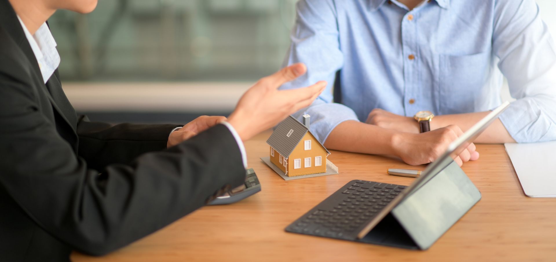 Business meeting with laptop, tablet, and a small house model on a wooden table
