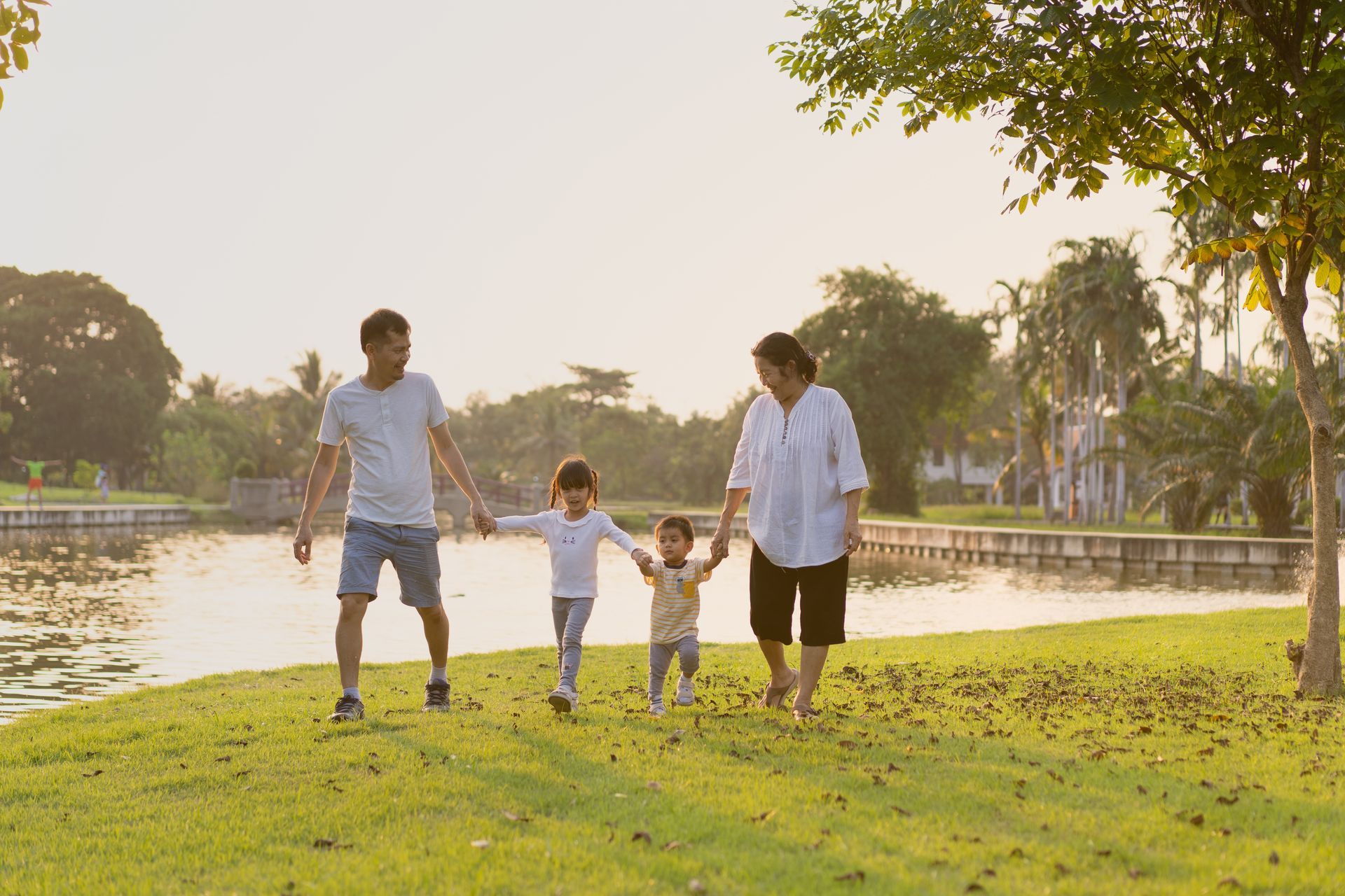 Family walking hand in hand along a grassy riverside path at sunset
