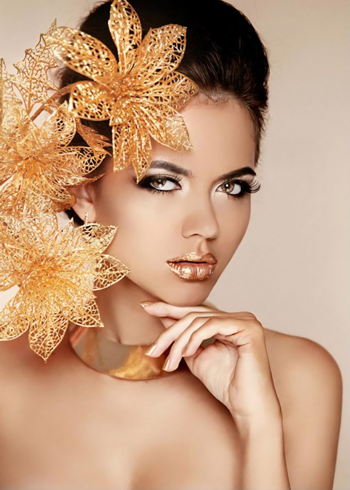 A person with metallic gold lips and hair ornaments made of intricate gold filigree, posing with a hand near their chin.