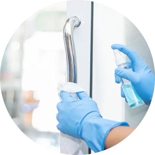 A person wearing blue gloves is cleaning a door handle with a spray bottle.