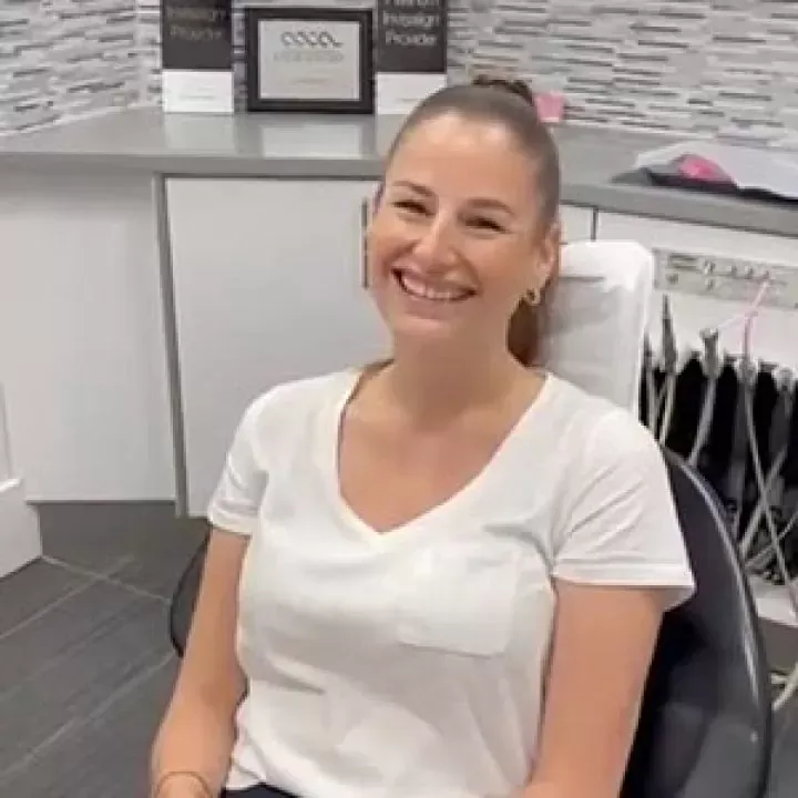 A woman is smiling while sitting in a dental chair.