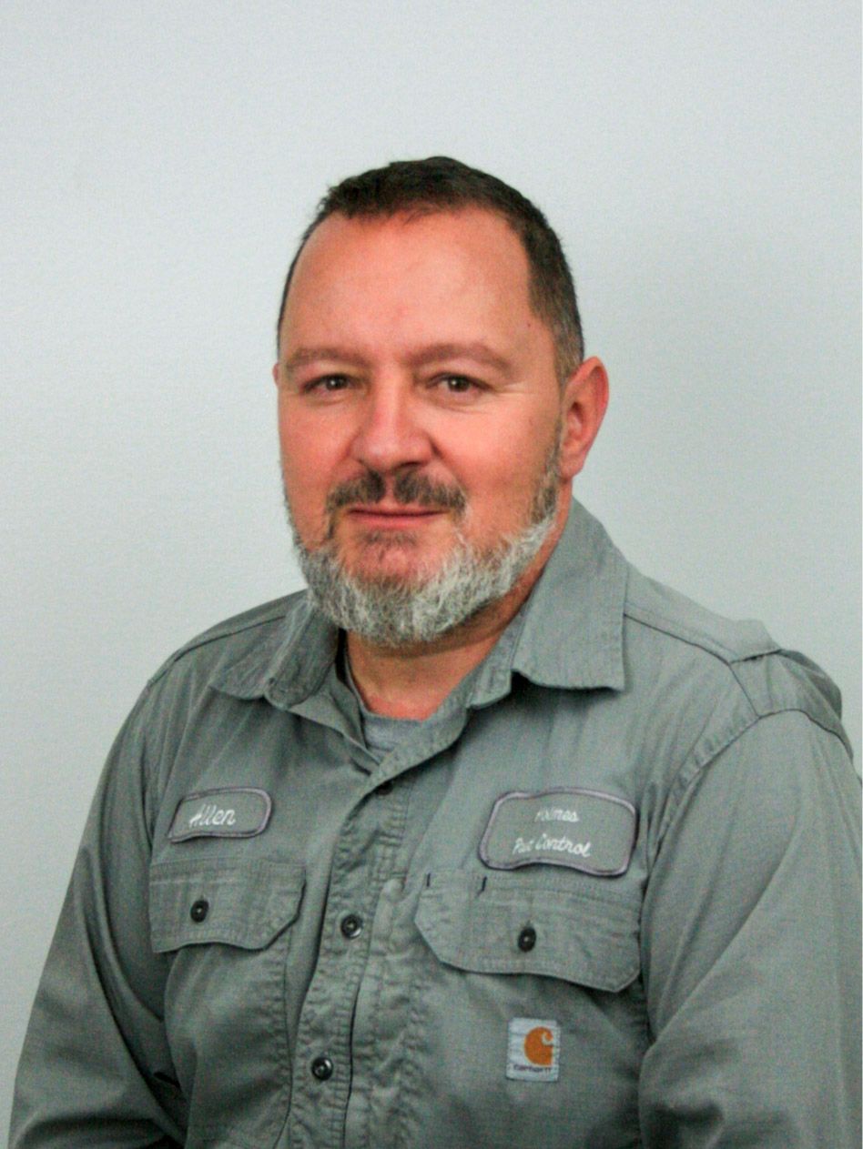 Man in gray work shirt with gray beard, smiling at the camera.