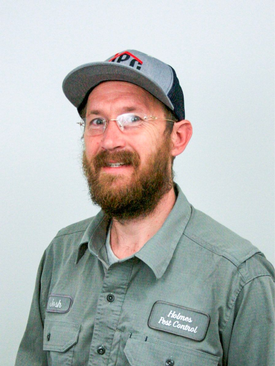 Man in glasses and cap, wearing a pest control uniform, smiling.