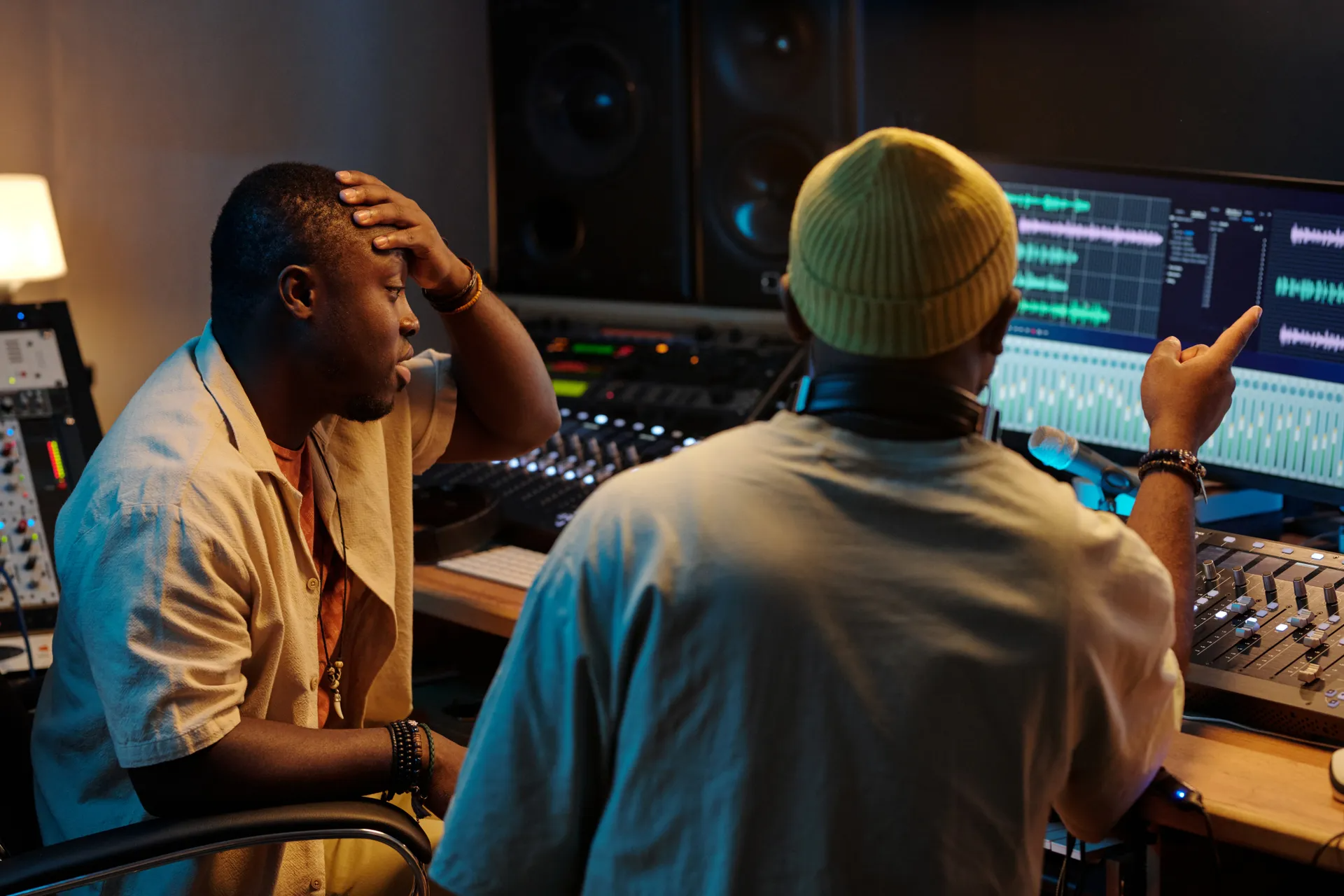 Two people in a recording studio adjust sound equipment and a music editing screen