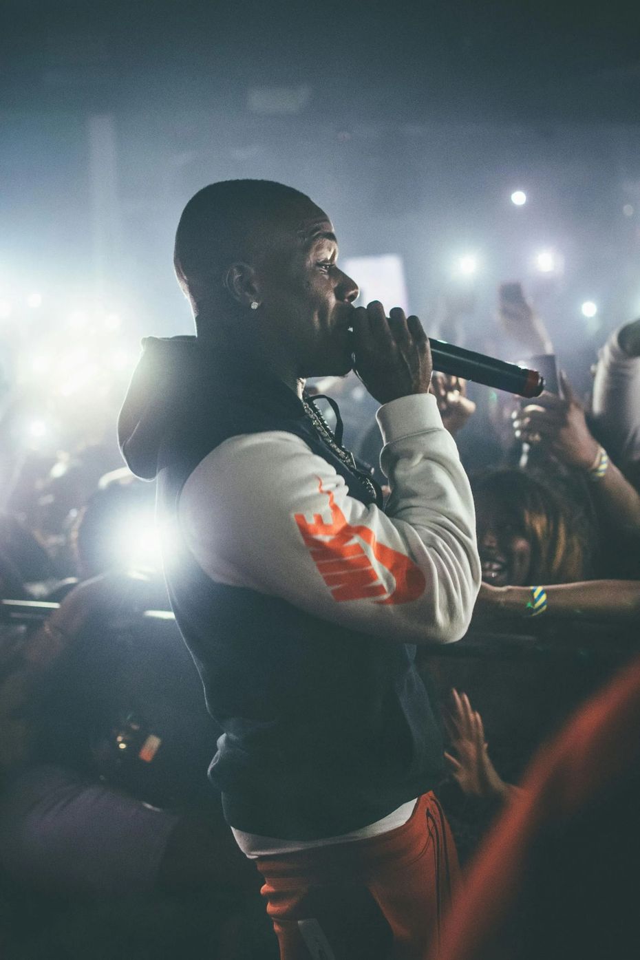 Singer performing on stage with a microphone, crowd holding up lights in the background.