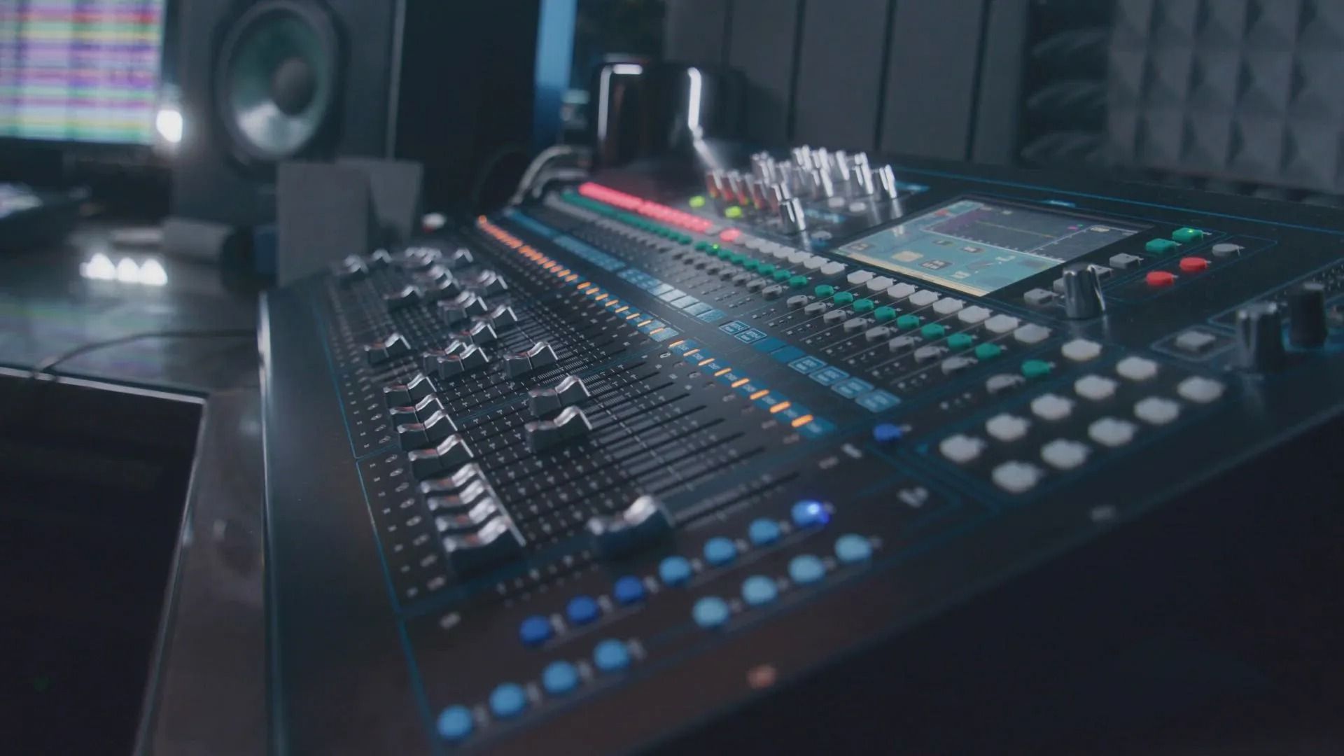 Audio mixing console with glowing lights and knobs in a dim studio setting