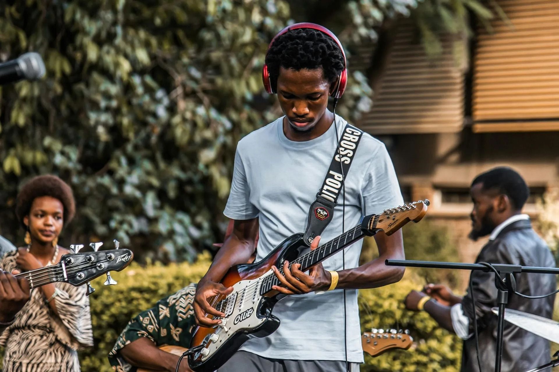 Band performing outdoors, with a guitarist in a gray shirt playing in the foreground.