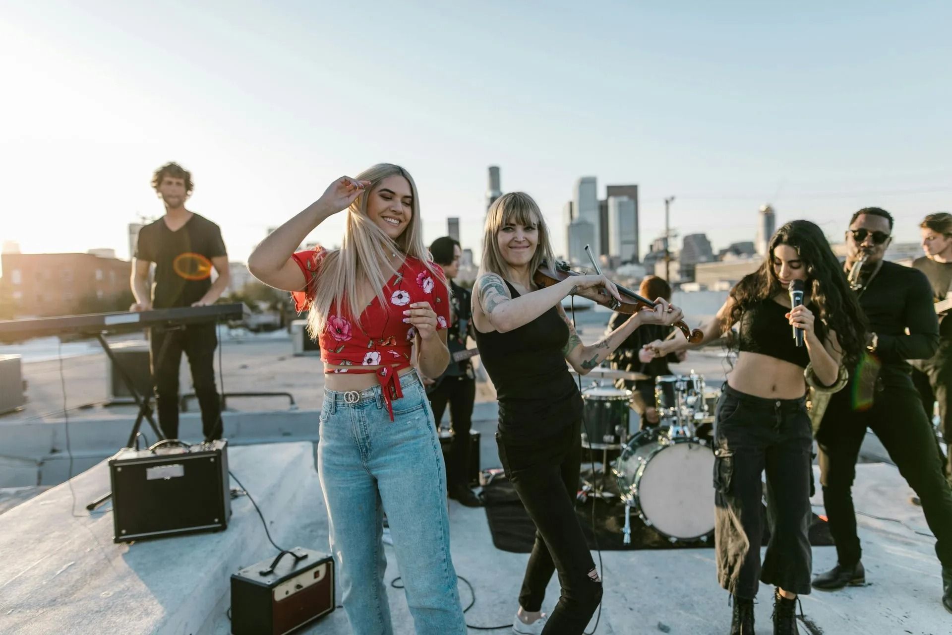 Band performing and dancing on a rooftop at sunset with city skyline in the background