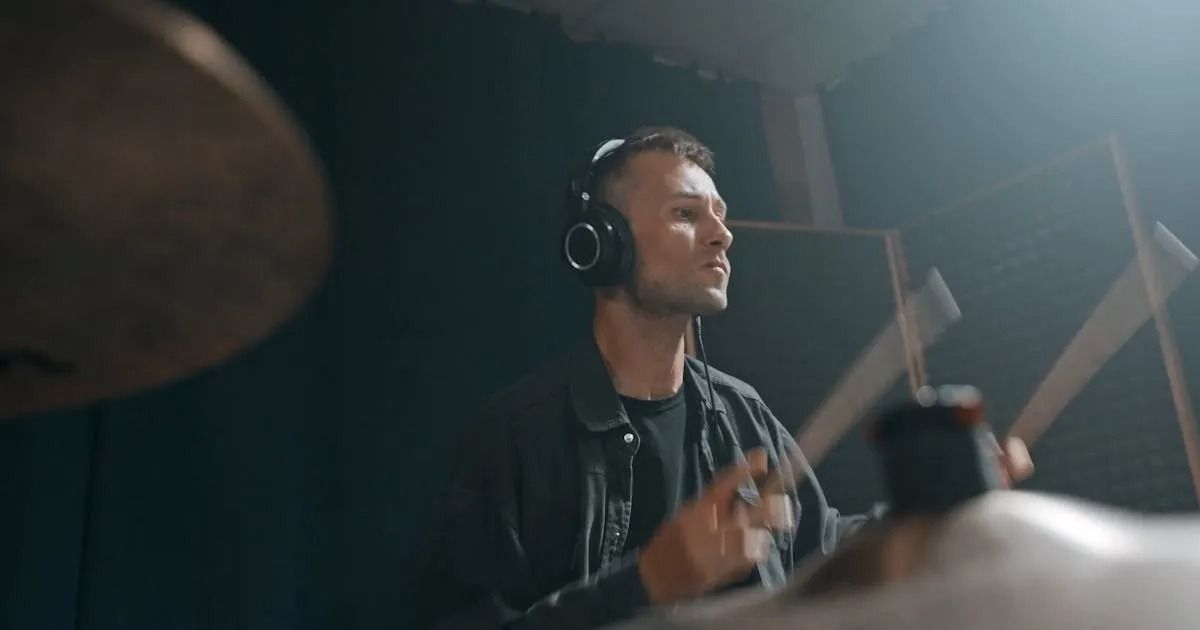 Drummer wearing headphones plays in a dim studio, blurred cymbals in the foreground.