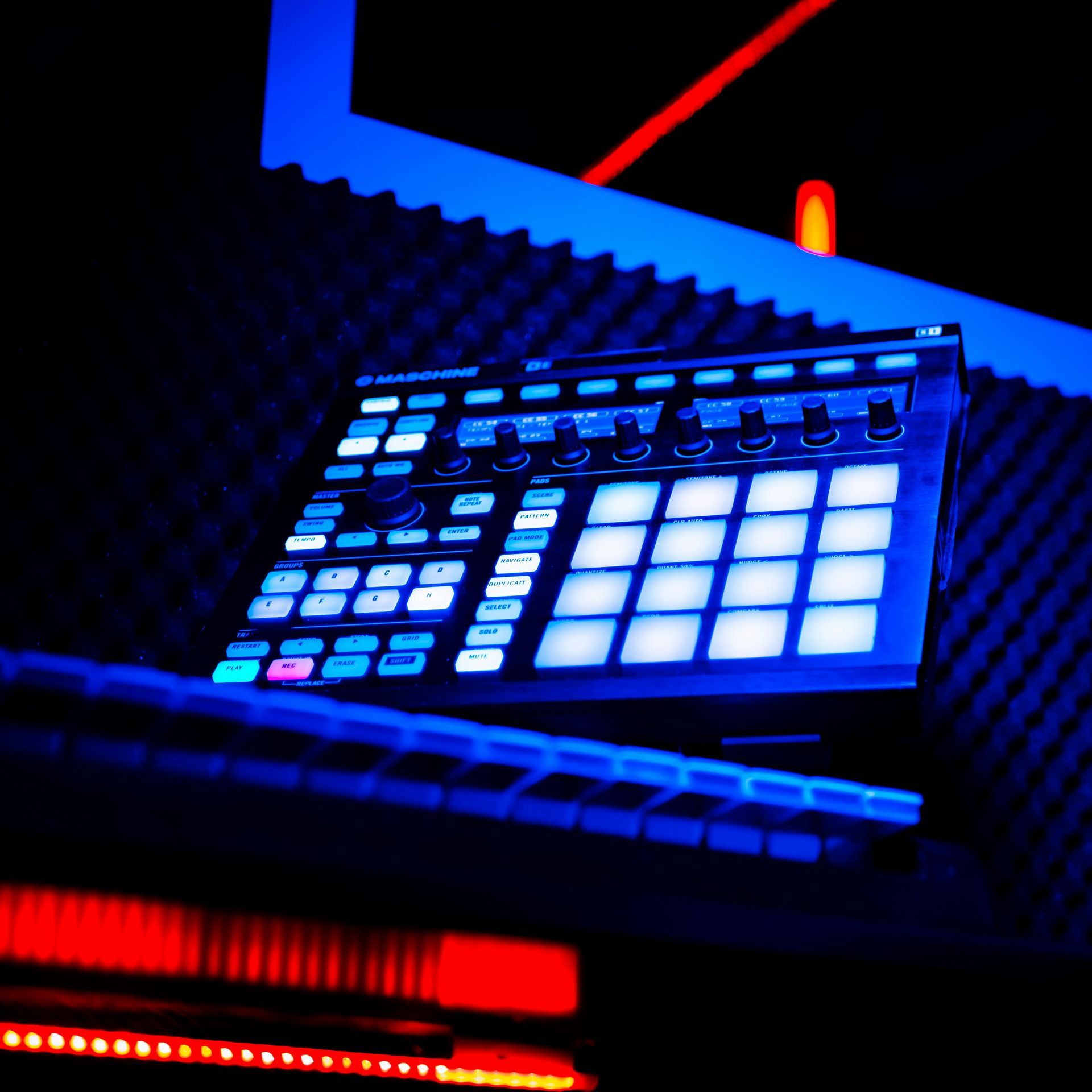 Blue-lit music production controller with illuminated pads and knobs in a dark studio