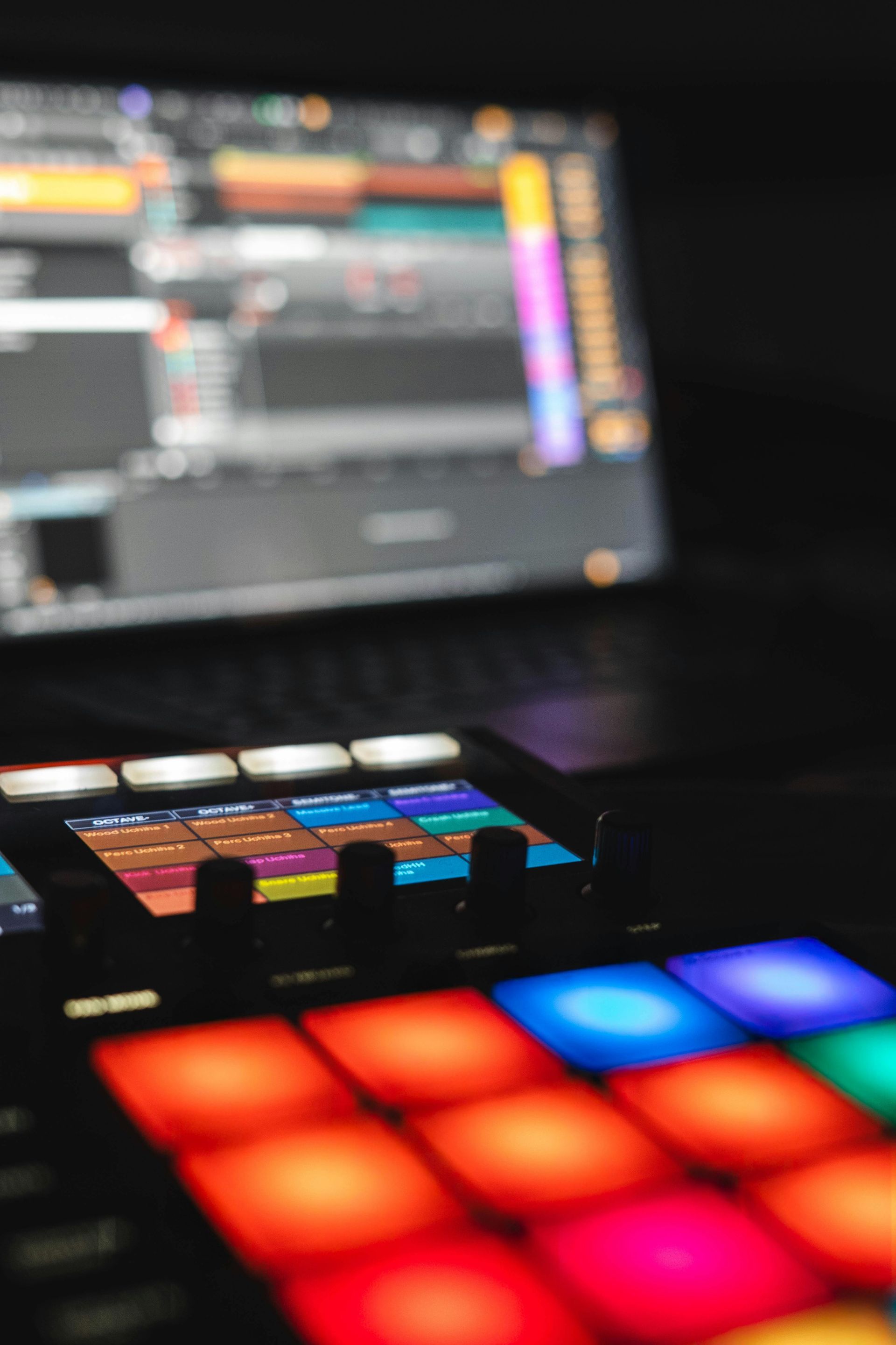 Colorful illuminated pad controller in front of a blurred laptop screen in a dim studio