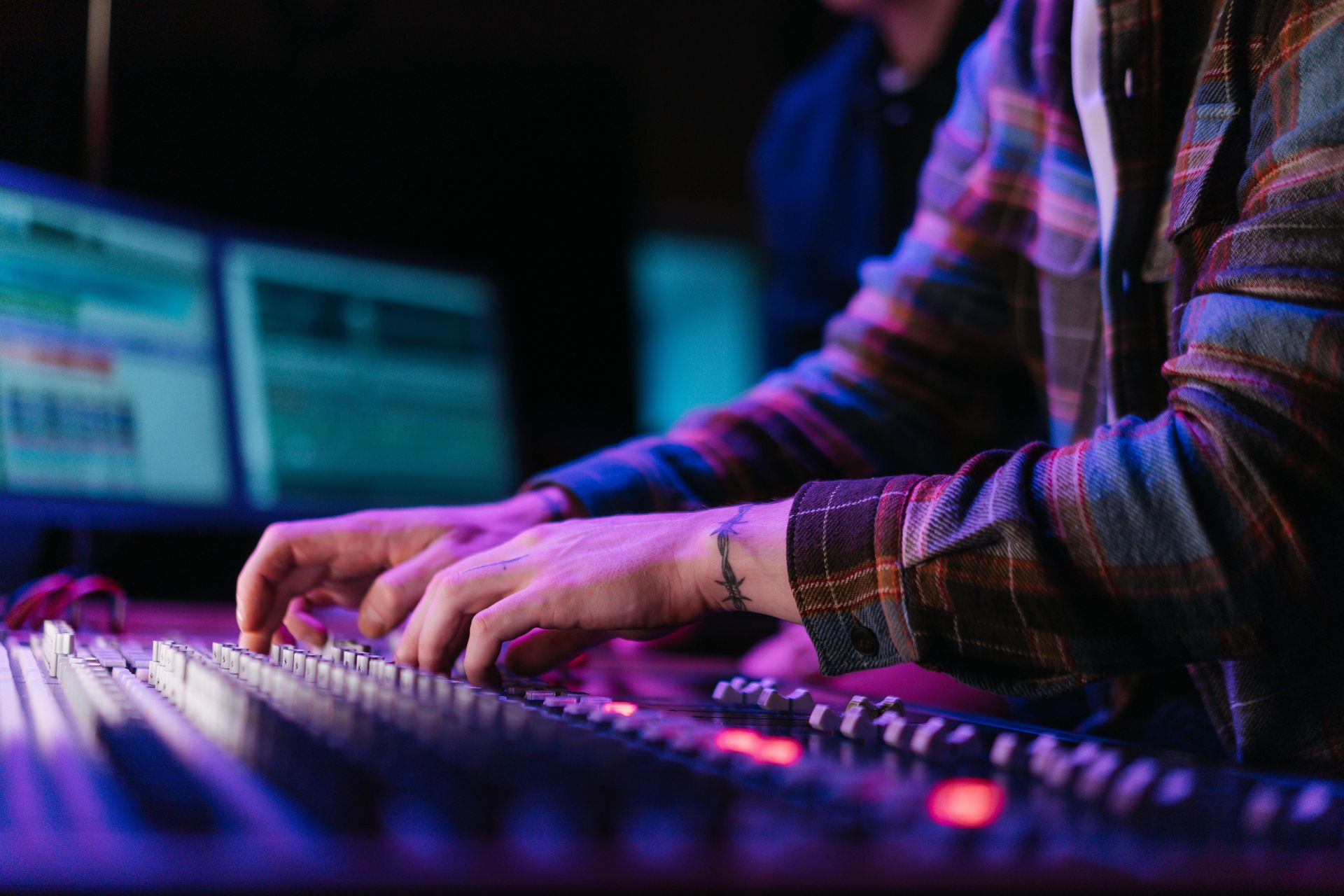 Hands adjusting controls on a mixing console in a neon-lit music studio