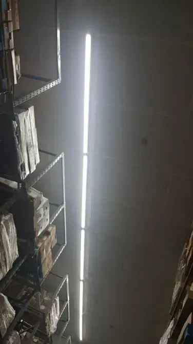 A store aisle with tall shelves and bright fluorescent ceiling lights, seen from below.