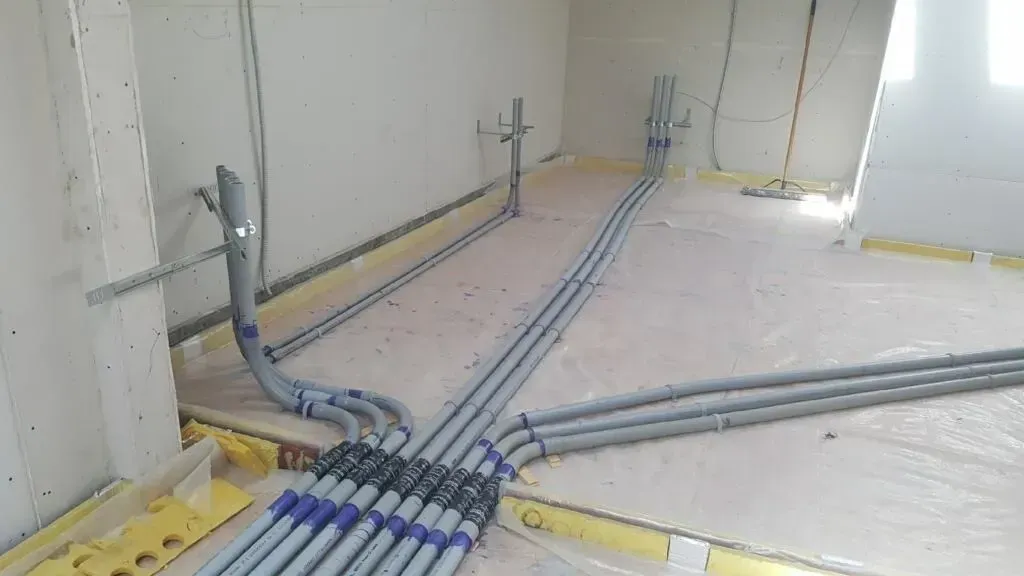 Gray conduit pipes laid in a wall and floor corner, showing electrical wiring installation under construction