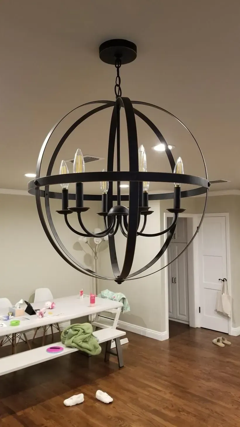 Black orb chandelier hanging in a dining room with a table and hardwood floor