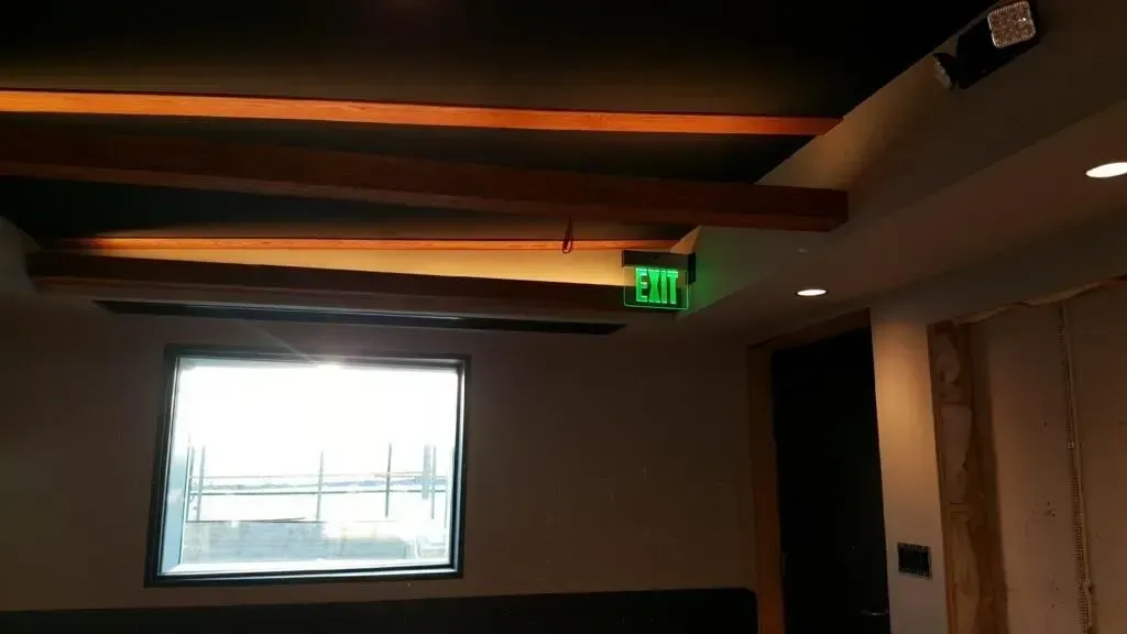 Dim room with a bright window, ceiling lights, and a green exit sign above a doorway.