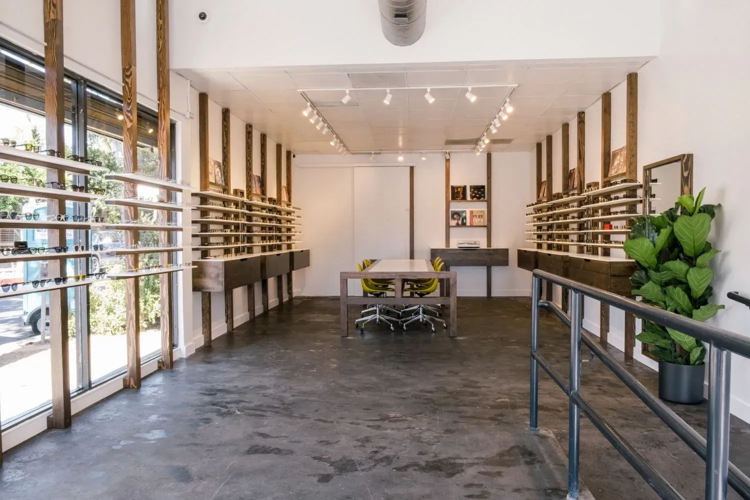 Modern retail interior with long shelves, metal display tables, and large windows along the left wall