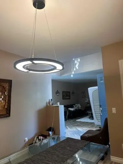 Modern dining room with a hanging ring light and a view into a living area beyond.